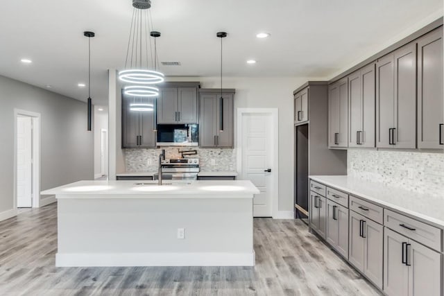 kitchen with decorative light fixtures, stainless steel appliances, light hardwood / wood-style floors, and an island with sink