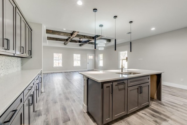 kitchen featuring light wood-type flooring, ceiling fan, a kitchen island with sink, sink, and pendant lighting