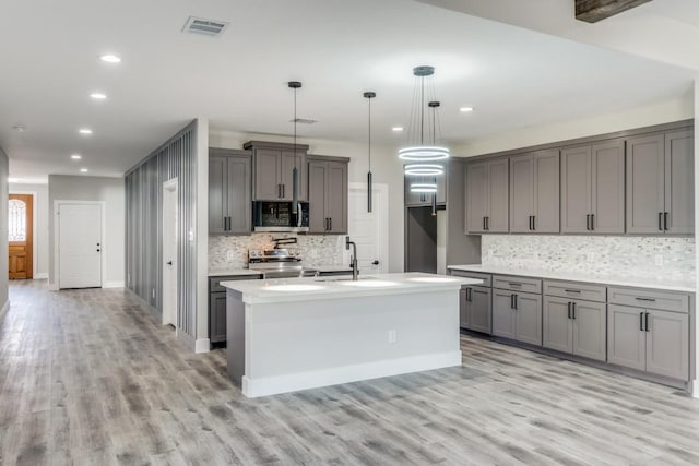 kitchen featuring gray cabinetry, hanging light fixtures, light wood-type flooring, tasteful backsplash, and stainless steel appliances