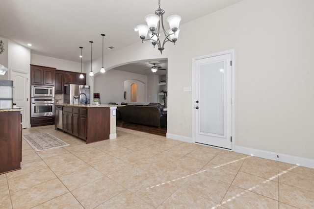 kitchen featuring dark brown cabinets, hanging light fixtures, light tile patterned floors, appliances with stainless steel finishes, and an island with sink