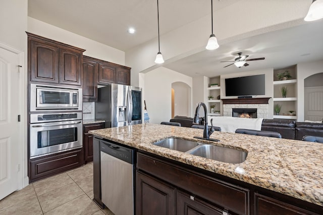 kitchen featuring dark brown cabinetry, appliances with stainless steel finishes, a stone fireplace, pendant lighting, and a sink