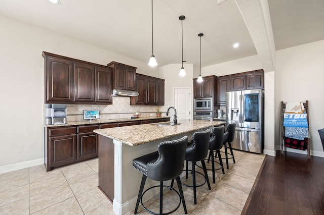 kitchen featuring tasteful backsplash, appliances with stainless steel finishes, a sink, dark brown cabinetry, and under cabinet range hood