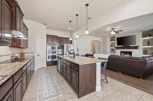 kitchen featuring light tile patterned floors, appliances with stainless steel finishes, a kitchen breakfast bar, under cabinet range hood, and a sink