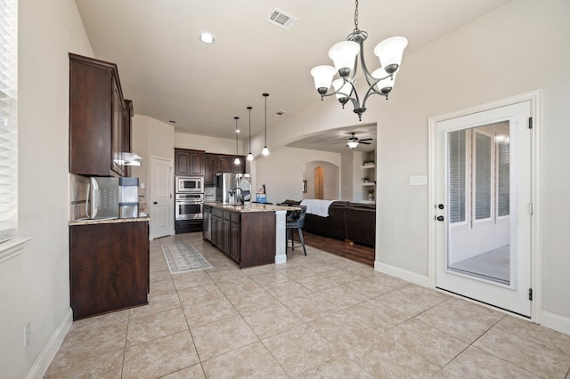 kitchen with arched walkways, a center island with sink, stainless steel appliances, open floor plan, and dark brown cabinetry