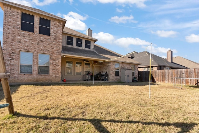 rear view of property with ceiling fan, an outbuilding, fence, a yard, and brick siding