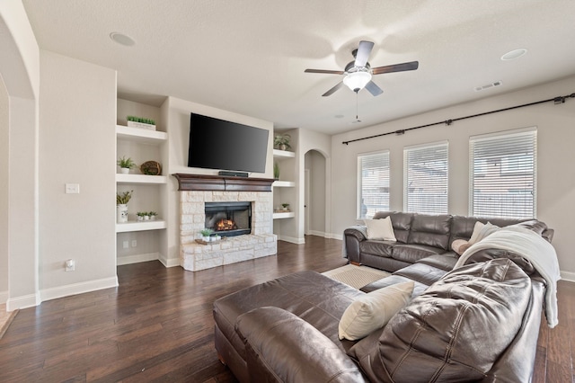 living room featuring visible vents, arched walkways, ceiling fan, wood finished floors, and a stone fireplace