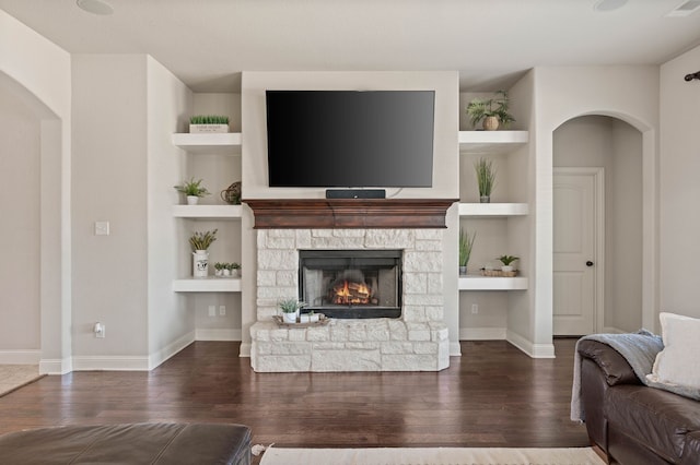 living area with arched walkways, a fireplace, wood finished floors, and built in features