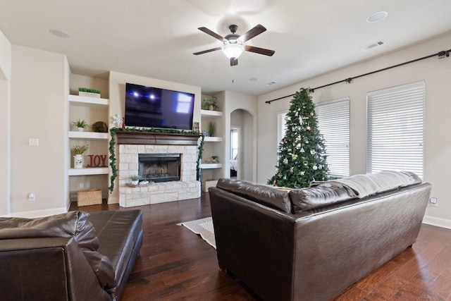 living room with built in features, ceiling fan, a fireplace, and dark hardwood / wood-style flooring