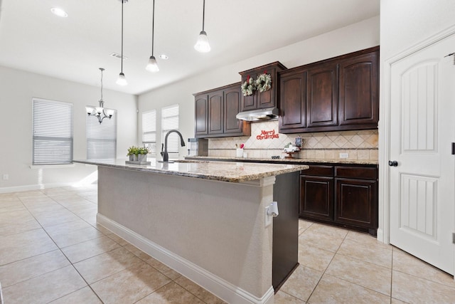 kitchen featuring sink, decorative light fixtures, dark brown cabinets, and a center island with sink