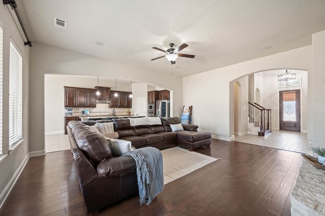 living area with arched walkways, dark wood-style flooring, ceiling fan, and stairway