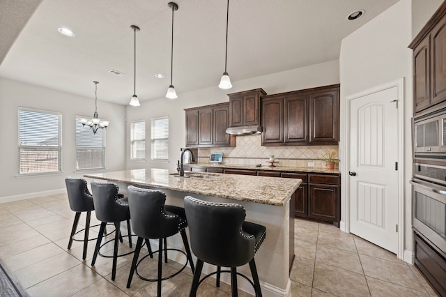 kitchen featuring a breakfast bar area, stainless steel appliances, backsplash, a sink, and under cabinet range hood