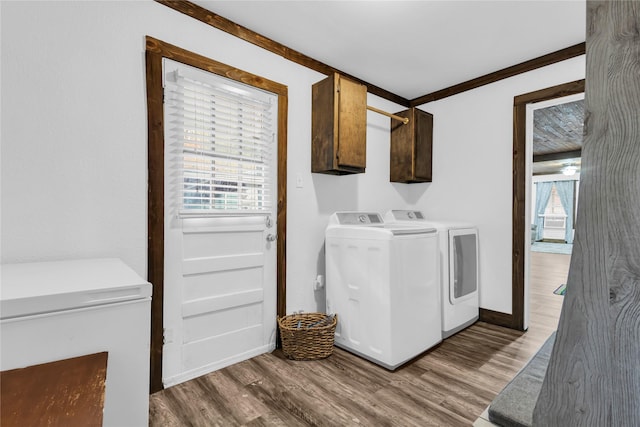 clothes washing area with washer and dryer, crown molding, cabinets, and wood-type flooring