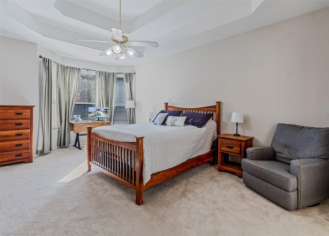 bedroom featuring light colored carpet, a raised ceiling, and ceiling fan