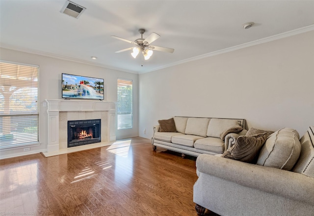 living room featuring a tiled fireplace, ceiling fan, hardwood / wood-style floors, and crown molding