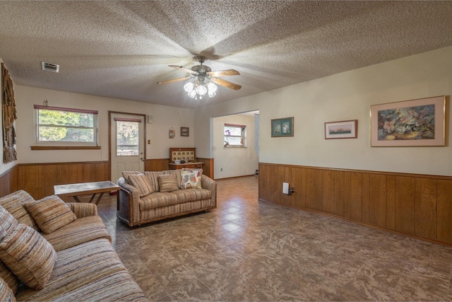 living room with ceiling fan, wood walls, and a textured ceiling