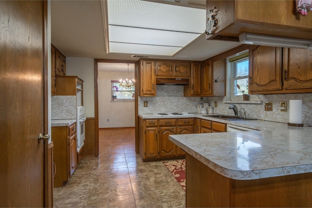 kitchen with kitchen peninsula, backsplash, white appliances, sink, and a notable chandelier