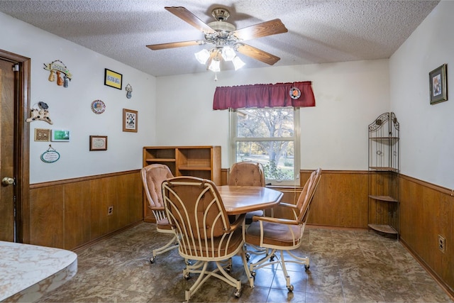 dining room featuring ceiling fan, wood walls, and a textured ceiling