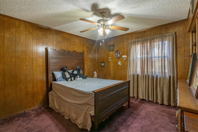 bedroom featuring ceiling fan, wooden walls, a textured ceiling, and dark colored carpet