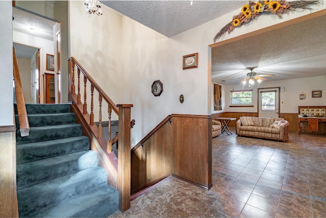 stairs with ceiling fan, a textured ceiling, and wooden walls