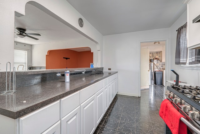 kitchen with white cabinetry, ceiling fan, stainless steel gas range, and sink