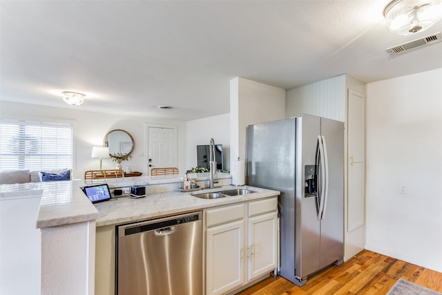 kitchen featuring kitchen peninsula, stainless steel appliances, sink, light hardwood / wood-style flooring, and white cabinetry