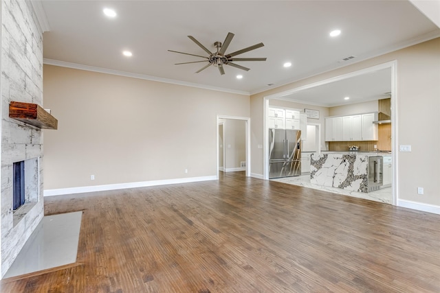 unfurnished living room featuring crown molding, wine cooler, ceiling fan, light wood-type flooring, and a fireplace