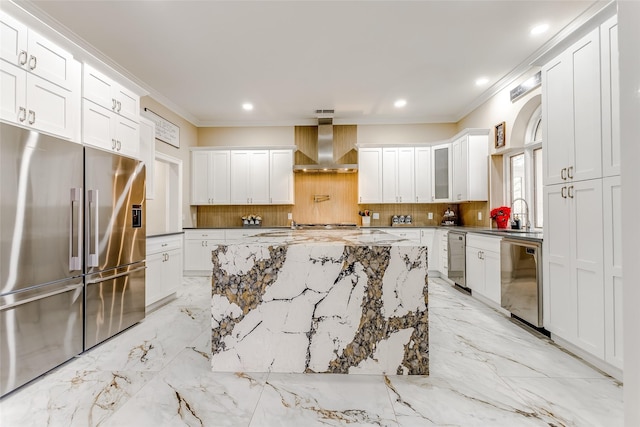 kitchen featuring appliances with stainless steel finishes, sink, wall chimney range hood, a center island, and white cabinetry