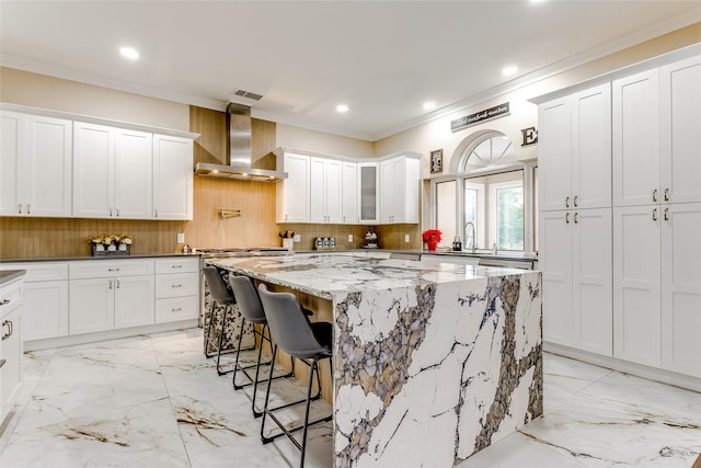 kitchen with a center island, white cabinets, a kitchen breakfast bar, wall chimney range hood, and light stone countertops