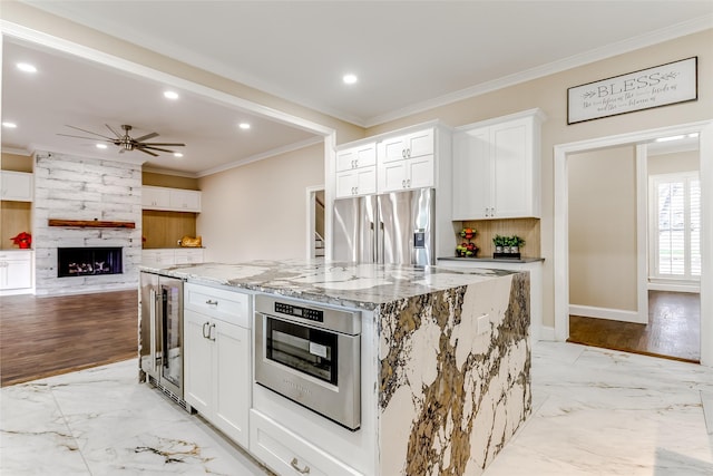 kitchen featuring light stone countertops, a kitchen island, white cabinetry, stainless steel appliances, and beverage cooler