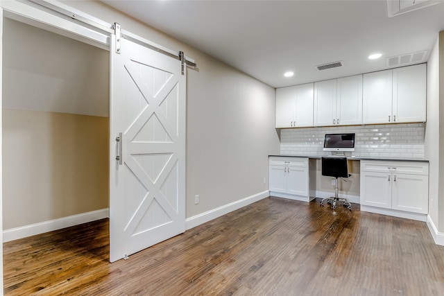 kitchen featuring backsplash, white cabinets, dark hardwood / wood-style floors, a barn door, and built in desk