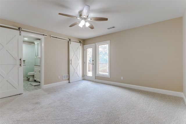 carpeted empty room featuring a barn door and ceiling fan