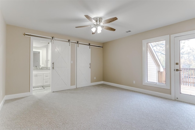 unfurnished bedroom with ceiling fan, a barn door, access to outside, and multiple windows