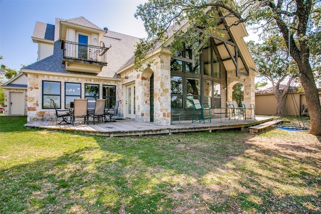 rear view of house with a balcony, a deck, and a lawn