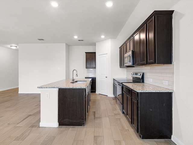 kitchen with light stone counters, stainless steel appliances, a kitchen island with sink, sink, and light hardwood / wood-style flooring