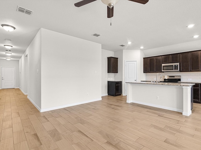 kitchen with a center island with sink, backsplash, stainless steel appliances, and light hardwood / wood-style flooring