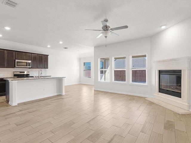 kitchen with stainless steel appliances, ceiling fan, sink, a fireplace, and light hardwood / wood-style floors