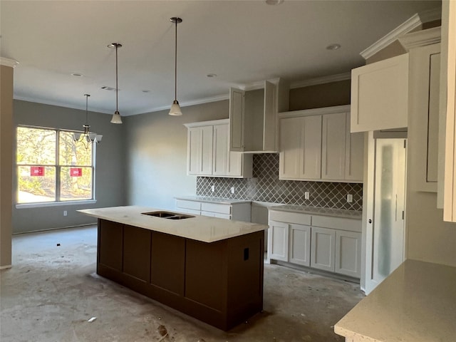 kitchen with decorative backsplash, ornamental molding, decorative light fixtures, a center island with sink, and white cabinetry