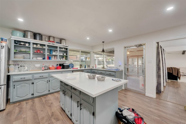 kitchen featuring backsplash, light hardwood / wood-style flooring, gray cabinets, a kitchen island, and hanging light fixtures