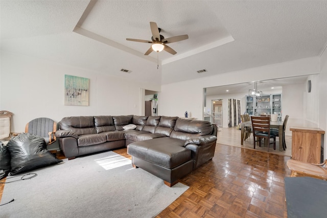 living room with a raised ceiling, dark parquet flooring, ceiling fan, and a textured ceiling