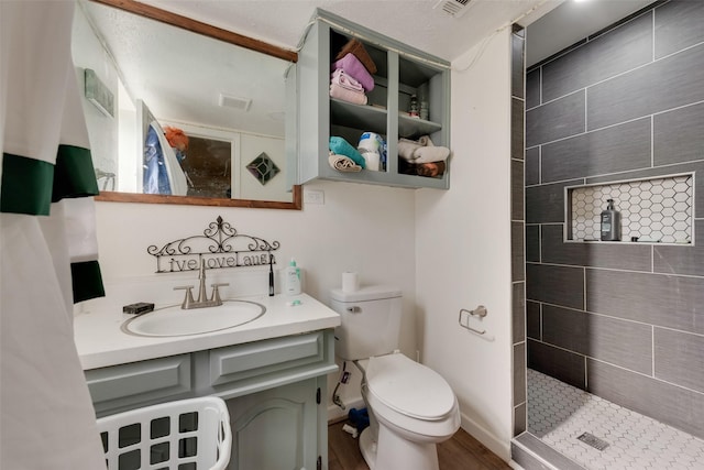 bathroom featuring toilet, vanity, hardwood / wood-style floors, and tiled shower