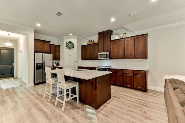 kitchen with a center island with sink, light hardwood / wood-style floors, a kitchen bar, and stainless steel appliances