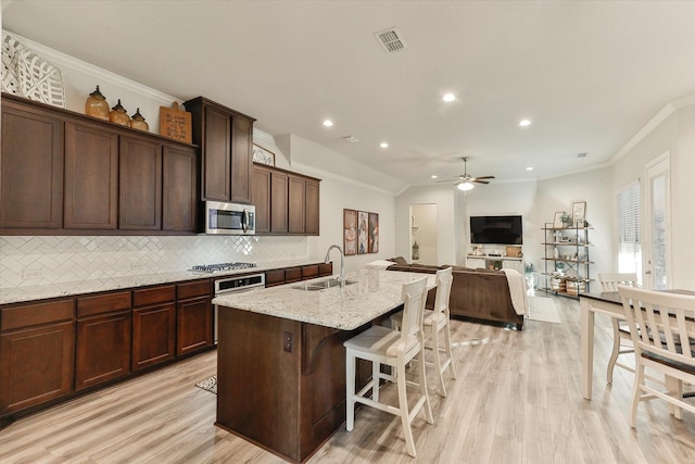 kitchen with a center island with sink, sink, light stone countertops, ornamental molding, and stainless steel appliances