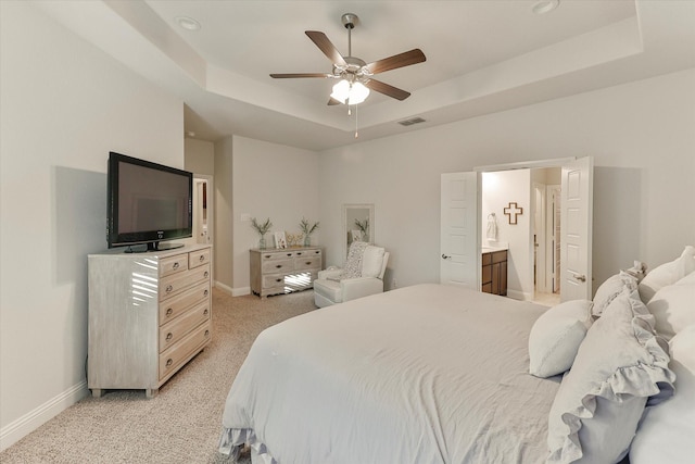 carpeted bedroom featuring a tray ceiling, connected bathroom, and ceiling fan