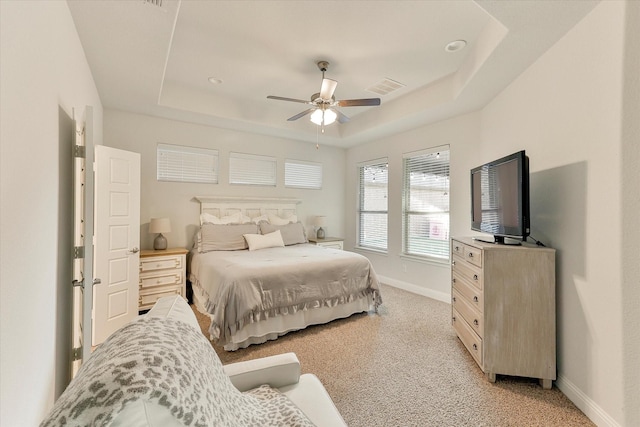 carpeted bedroom with a raised ceiling and ceiling fan