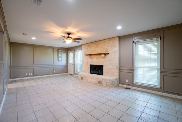 508 Squires Ln, Krugerville, TX 76227 - unfurnished living room featuring ceiling fan, a stone fireplace, visible vents, light tile patterned floors, and a decorative wall