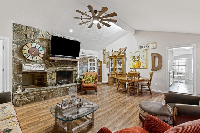 living room with a stone fireplace, vaulted ceiling with beams, ceiling fan, a textured ceiling, and wood-type flooring