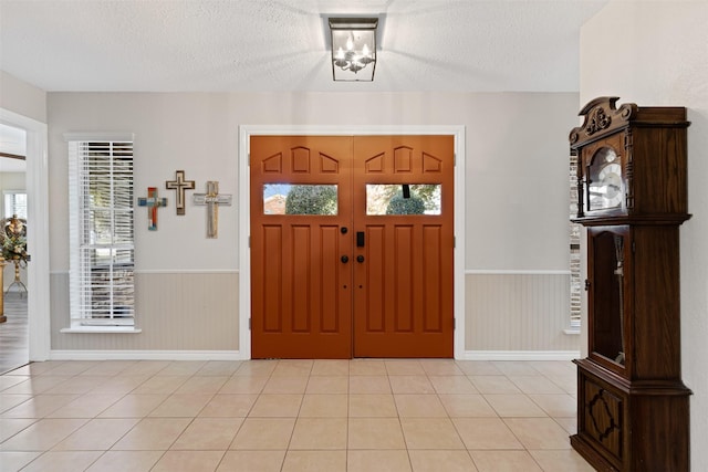 entrance foyer with wooden walls, light tile patterned floors, a textured ceiling, and a notable chandelier