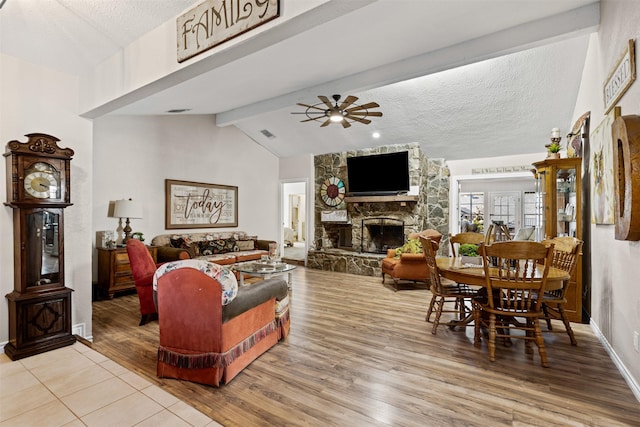 living room with a textured ceiling, ceiling fan, lofted ceiling with beams, a fireplace, and light hardwood / wood-style floors