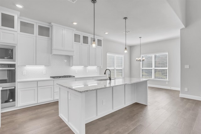 kitchen featuring light stone countertops, stainless steel appliances, white cabinetry, and an island with sink