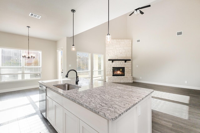 kitchen with light stone counters, a sink, visible vents, white cabinets, and hanging light fixtures